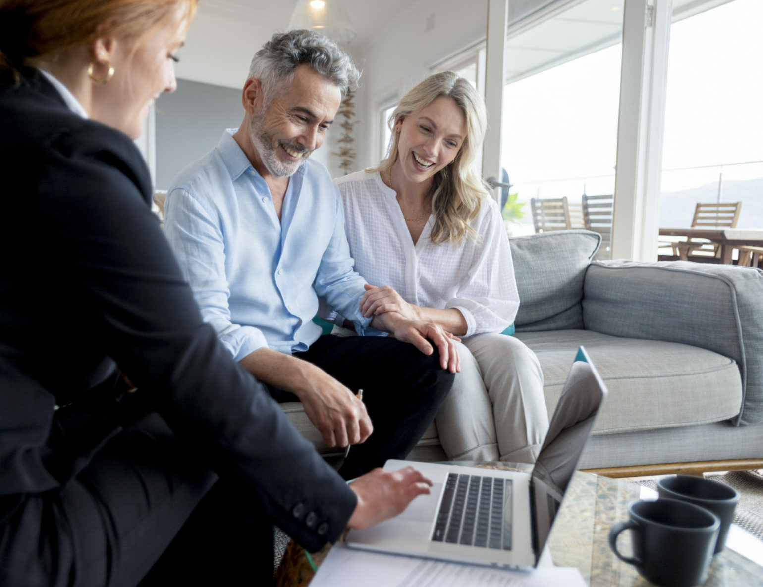 Heureux couple d'âge mûr rencontrant un conseiller en investissements et en finances à la maison. Ils sont heureux et souriants. Le conseiller utilise un ordinateur portable.